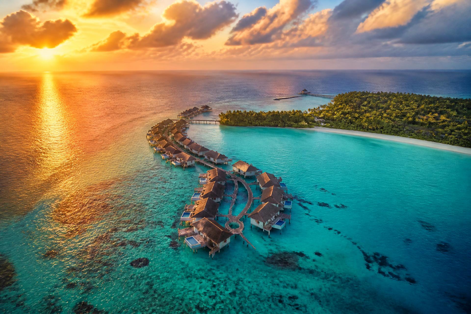 Aerial view of overwater villas above a turquoise lagoon at sunset